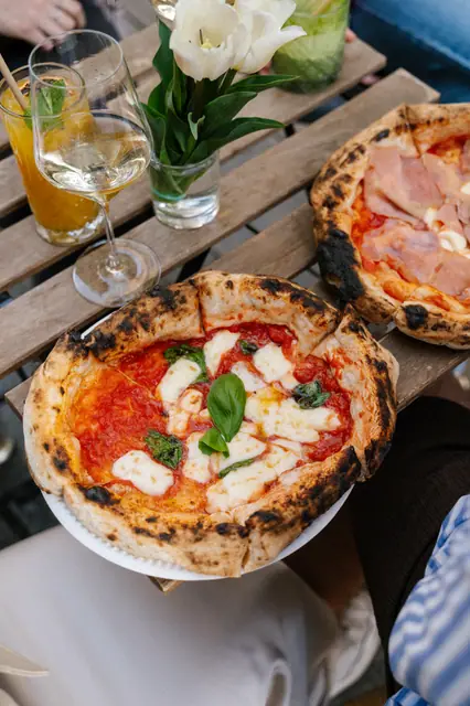 Margherita a pizza se šunkou na stolku s drinky a květinami