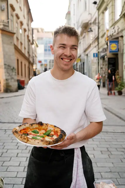Pizzaiolo s pizzou v ruce uprostřed dlážděné ulice v centru Brna