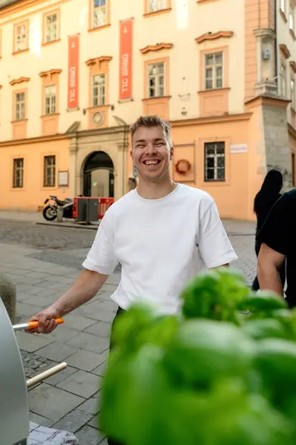 Smějící se pizzaiolo u pece, v popředí bazalka