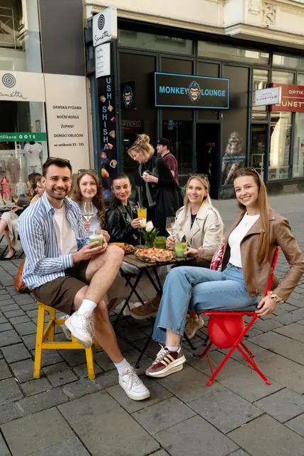 Parta přátel u stolku s pizzou a drinky v centru Brna