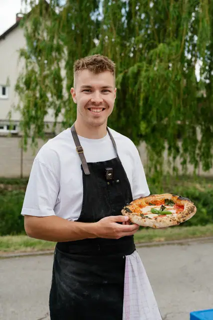 Pizzaiolo Adam Kaňa se usmívá s čerstvě upečenou pizzou v ruce