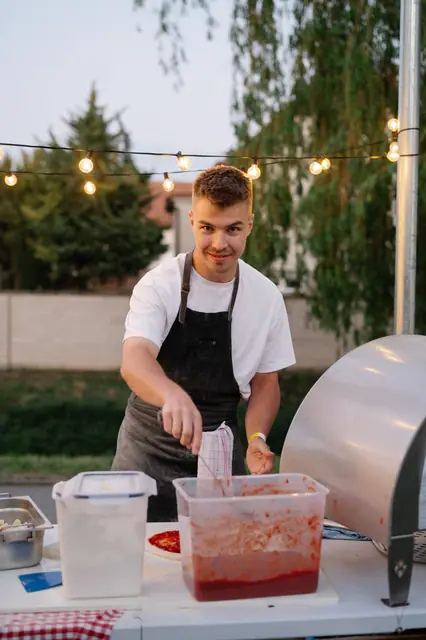Pizzaiolo u stánku pod světýlky rozetírá rajčatový základ