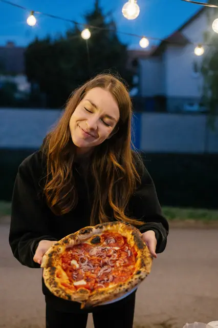 Hostka s pizzou pod řetězem rozsvícených žárovek na večerním pop-upu