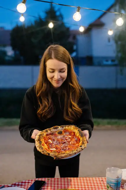 Hostka drží pizzu pod řetězem rozsvícených žárovek na večerním pop-upu