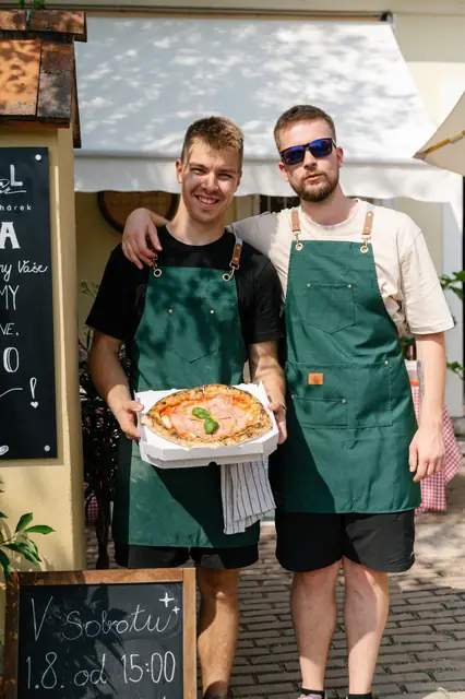 Dva pizzaioli s pizzou před vchodem do kavárny Knoll