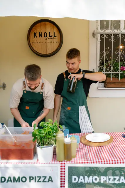 Pizzaioli připravují pizzu u stánku pod cedulí Knoll