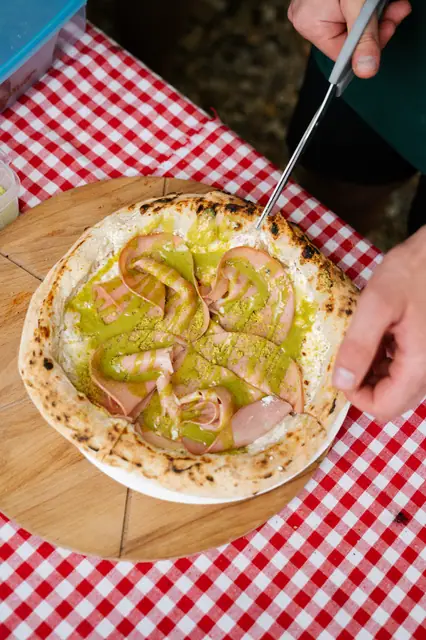 Krájení pizzy s mortadelou a pistáciovým pestem na kostkovaném ubrusu